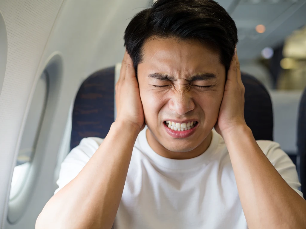 Man experiencing airplane ear pain caused by ear barotrauma during a flight.